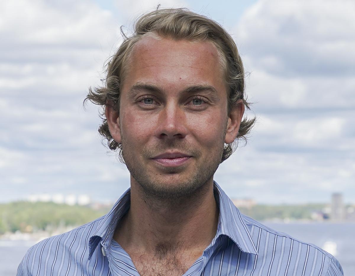 Porträtt av Tom Andersson, Sustainability Communication Manager på Dustin, som ler utomhus vid vattnet