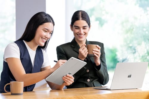 Twee collega’s werken samen met een Surface Pro en een Surface Laptop in een helder kantoor.