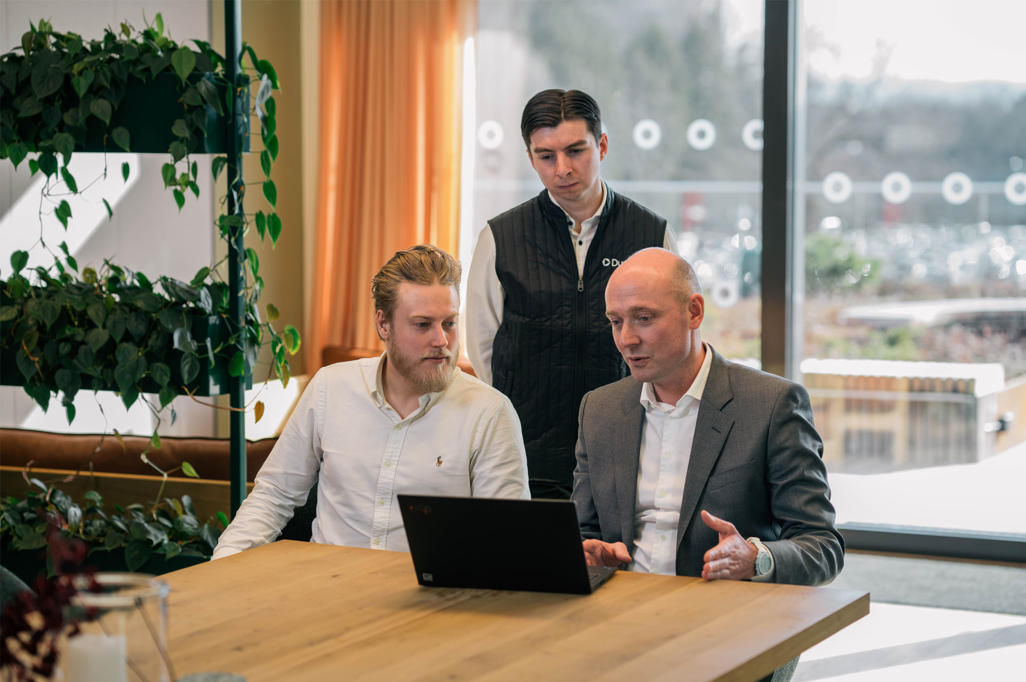 The interviewees look at a laptop, while one of them is explaining something.