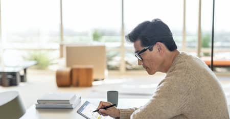 Un homme est assis dans un café avec un ordinateur portable et une tasse de café, souriant en regardant par la fenêtre.