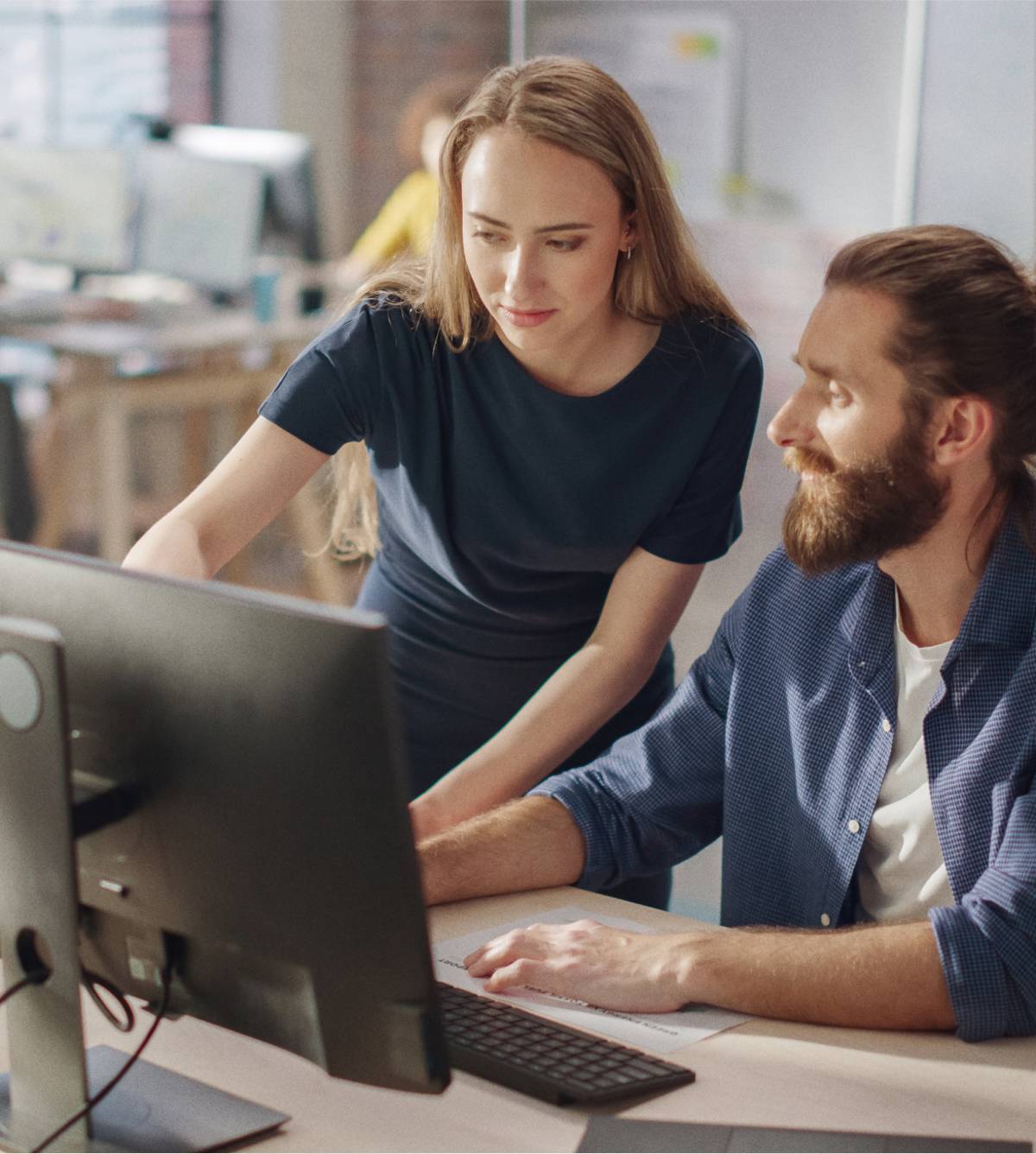 In een moderne kantoorruimte werken twee collega’s samen aan een bureau; ze kijken naar grafieken op een computermonitor.
