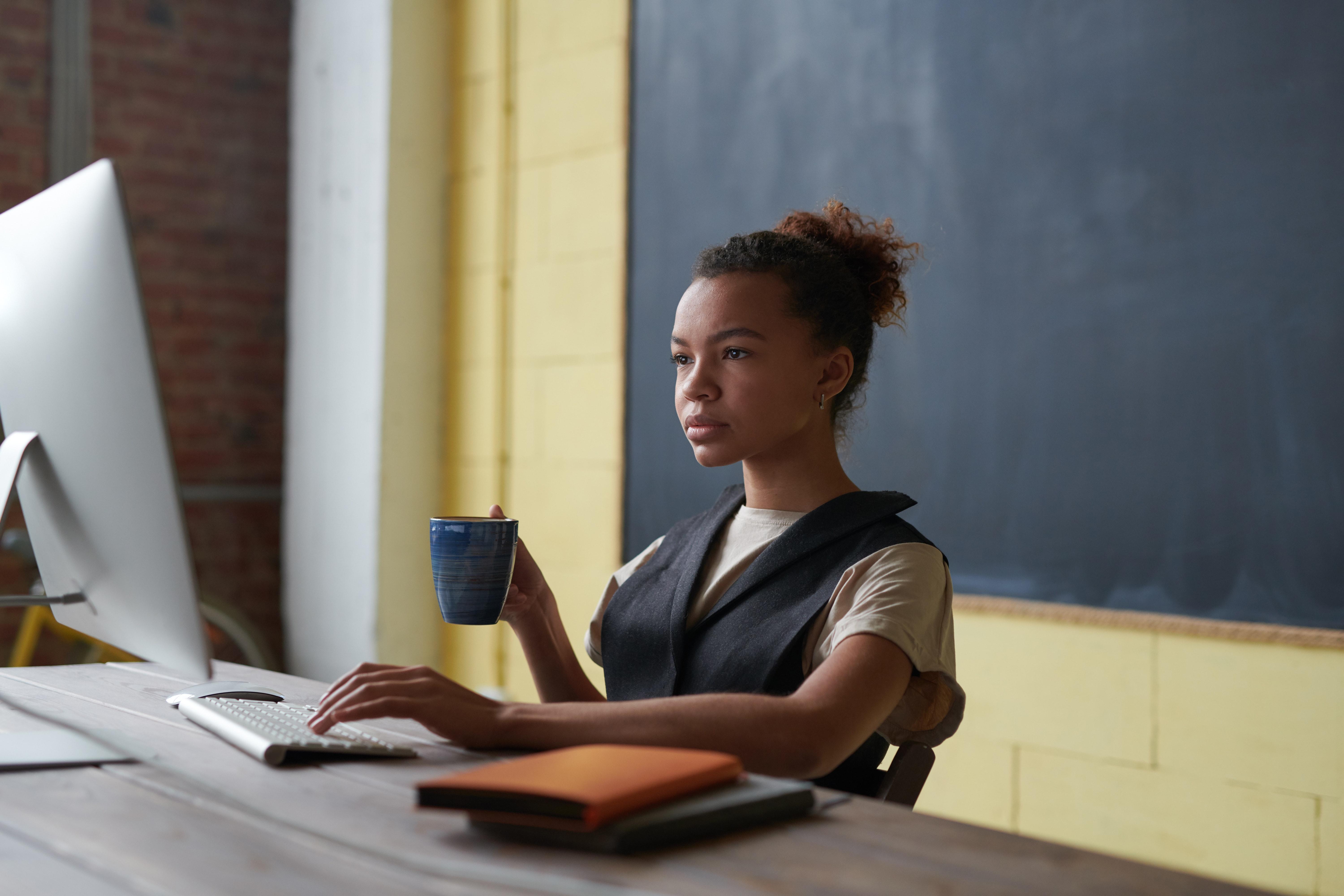 female teacher sitting by desk with computer screen in classroom