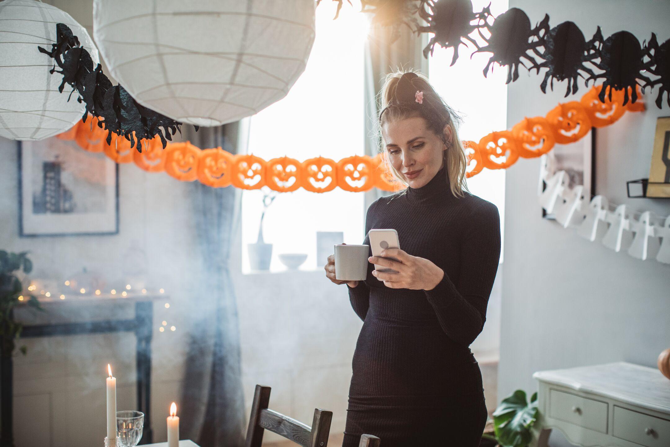 woman surrounded by halloween decorations looking at phone