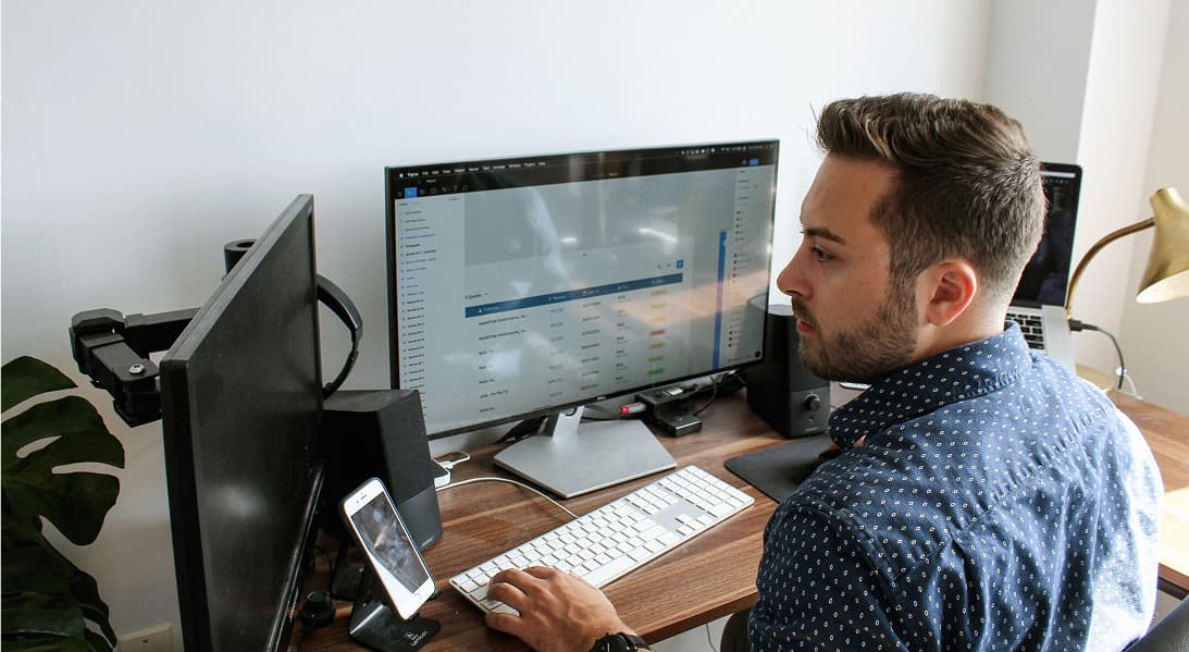 En redovisningsekonom vid en arbetsstation med dubbla bildskärmar, som granskar finansiella data och bokföringsprogramvara.