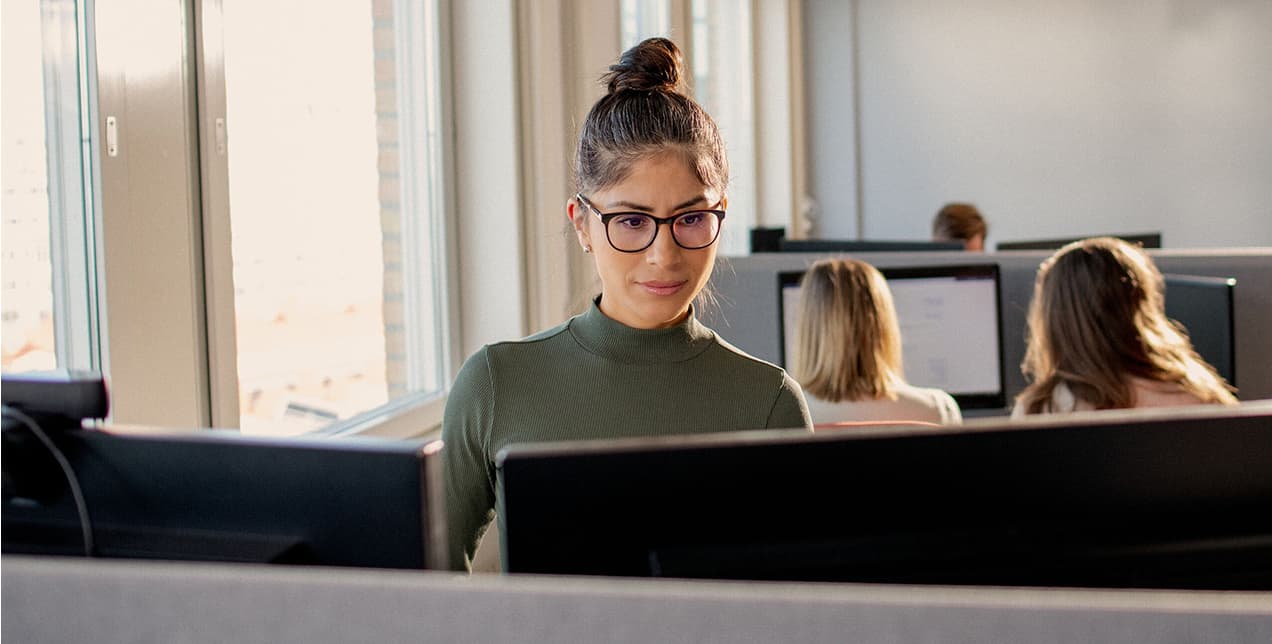 Kvinde, der arbejder ved flere computerskærme i et kontormiljø.
